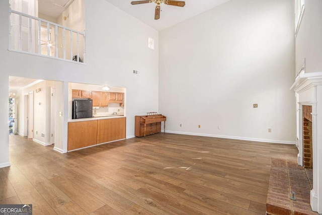 unfurnished living room with high vaulted ceiling, a ceiling fan, hardwood / wood-style flooring, a fireplace, and baseboards