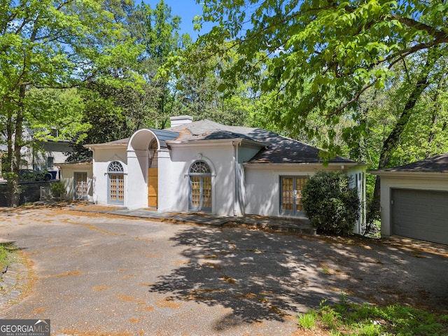 view of front of property with a chimney, stucco siding, driveway, french doors, and a garage