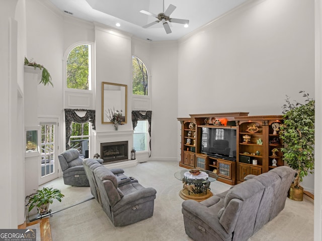 carpeted living room with crown molding, a towering ceiling, baseboards, a fireplace with raised hearth, and a ceiling fan