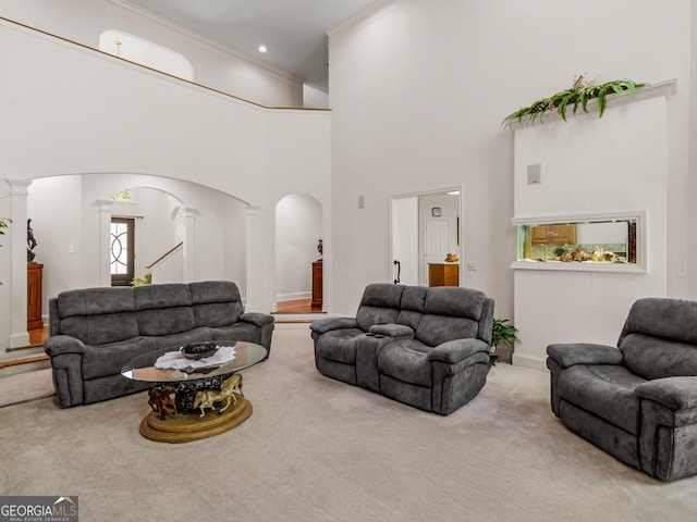carpeted living area featuring crown molding, arched walkways, baseboards, a towering ceiling, and ornate columns