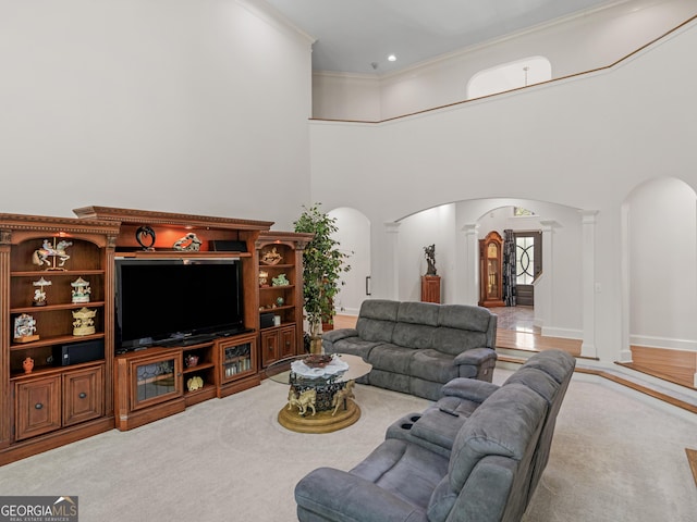 carpeted living area with crown molding, arched walkways, decorative columns, and a towering ceiling