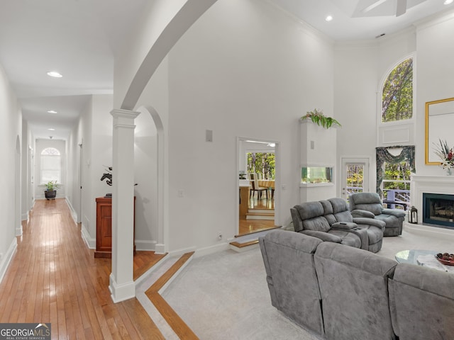living area with light wood-style floors, arched walkways, a fireplace with raised hearth, and a wealth of natural light