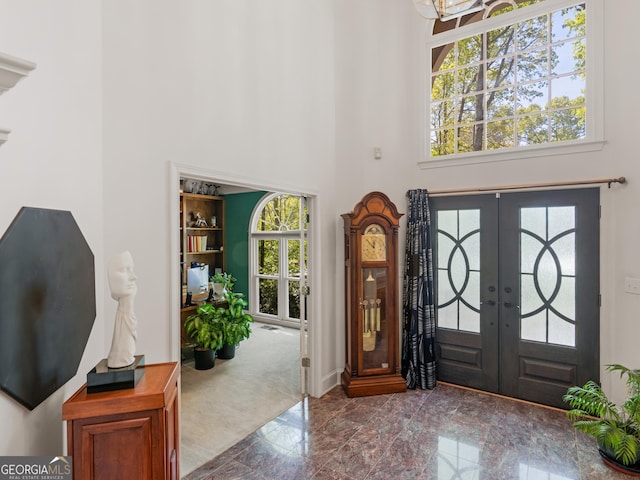 entryway featuring french doors, marble finish floor, a towering ceiling, and baseboards