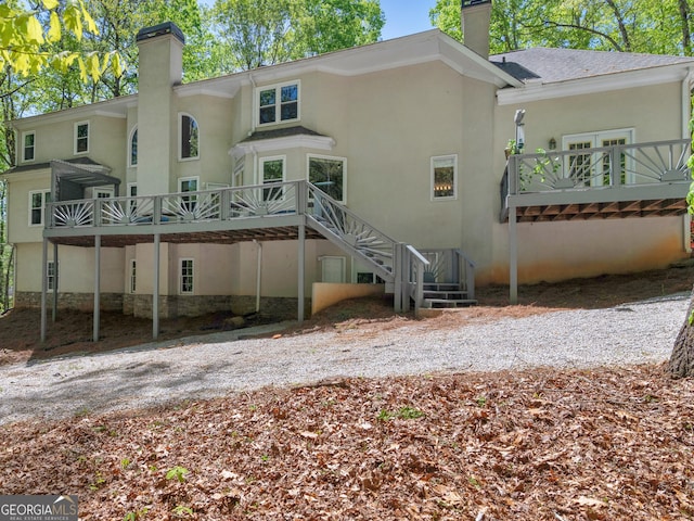 back of house featuring stairs, stucco siding, a chimney, and a deck