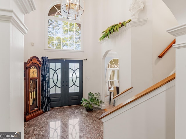 entryway with a high ceiling, arched walkways, a chandelier, french doors, and stairway