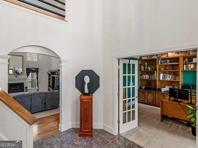 interior space featuring a high ceiling, a fireplace, arched walkways, baseboards, and decorative columns