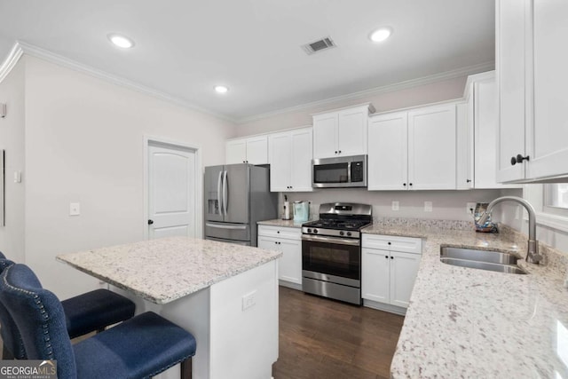 kitchen featuring a sink, a breakfast bar, stainless steel appliances, ornamental molding, and visible vents