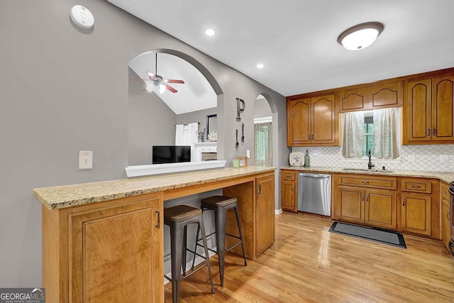 kitchen featuring lofted ceiling, dishwasher, brown cabinetry, arched walkways, and backsplash