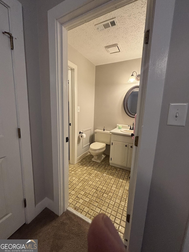 half bath with toilet, a textured ceiling, vanity, and baseboards