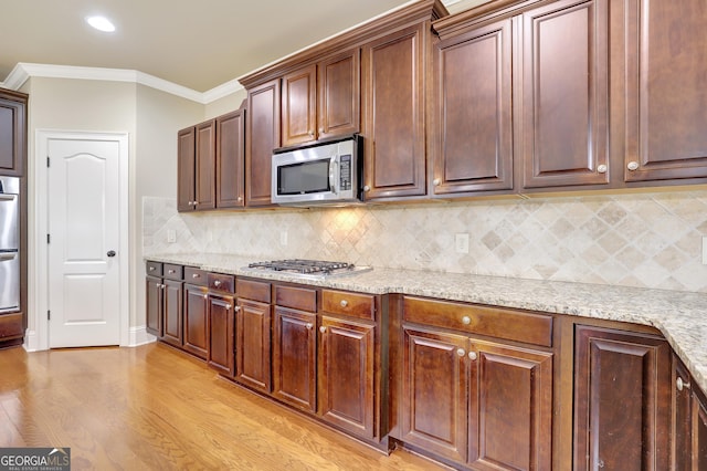 kitchen featuring light stone counters, stainless steel appliances, ornamental molding, decorative backsplash, and light wood-style flooring