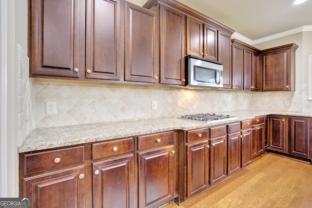 kitchen featuring light stone counters, ornamental molding, decorative backsplash, light wood-style flooring, and appliances with stainless steel finishes