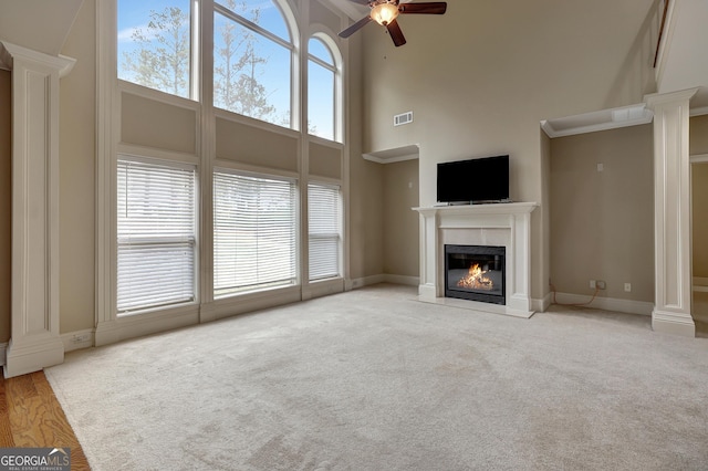 unfurnished living room featuring visible vents, a towering ceiling, carpet, ceiling fan, and a high end fireplace