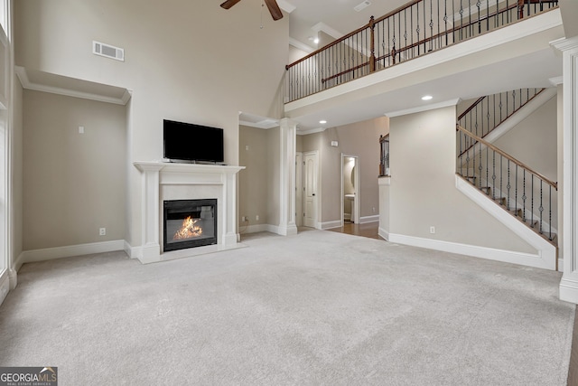 unfurnished living room featuring a glass covered fireplace, a high ceiling, a ceiling fan, and carpet flooring