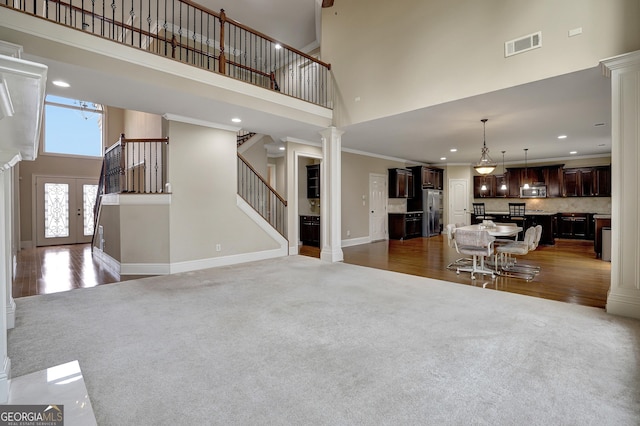 unfurnished living room with light wood finished floors, decorative columns, visible vents, a high ceiling, and stairs