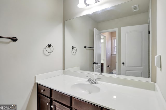 bathroom with toilet, vanity, and visible vents