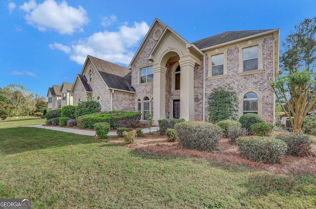 french provincial home with a front lawn, brick siding, and roof with shingles