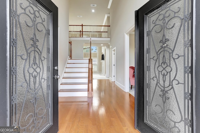 entryway featuring stairway, a high ceiling, wood finished floors, visible vents, and baseboards