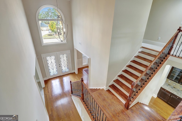 entryway with french doors, light wood-style flooring, visible vents, a towering ceiling, and stairway
