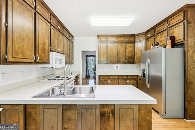 kitchen featuring a peninsula, light wood-style floors, backsplash, white appliances, and light countertops