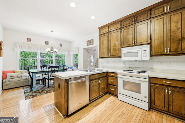 kitchen with a sink, white appliances, an inviting chandelier, light countertops, and a peninsula