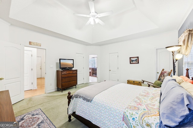 bedroom featuring a raised ceiling, a ceiling fan, ornamental molding, ensuite bath, and light colored carpet
