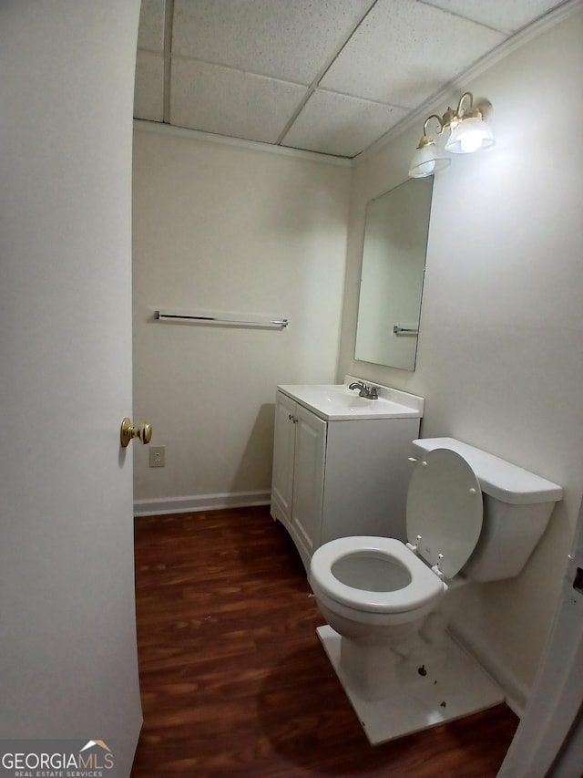 half bathroom featuring toilet, a drop ceiling, baseboards, wood finished floors, and vanity
