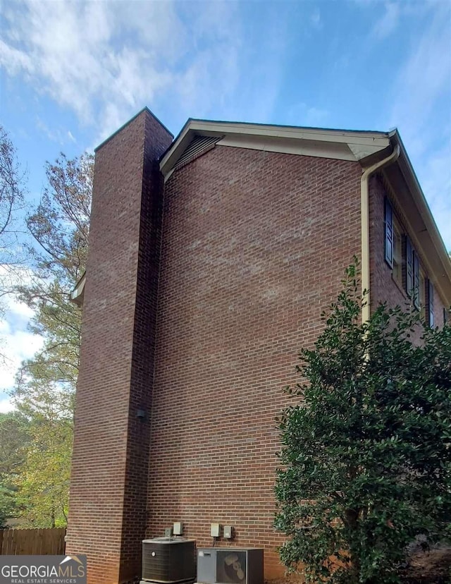 view of property exterior featuring fence, a chimney, brick siding, and central air condition unit