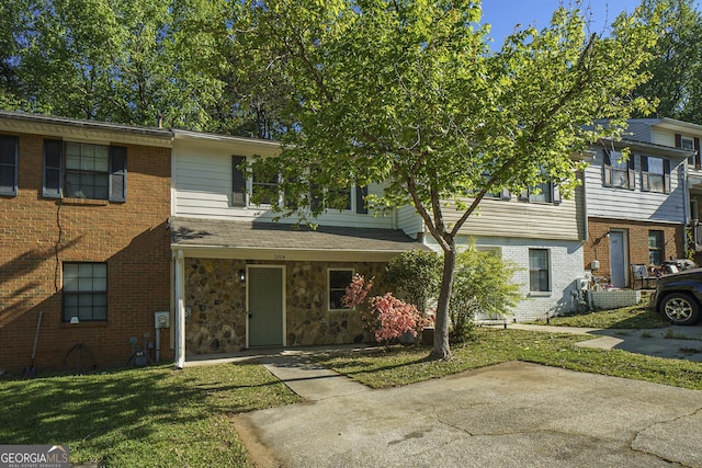 townhome / multi-family property featuring a front yard, stone siding, and brick siding