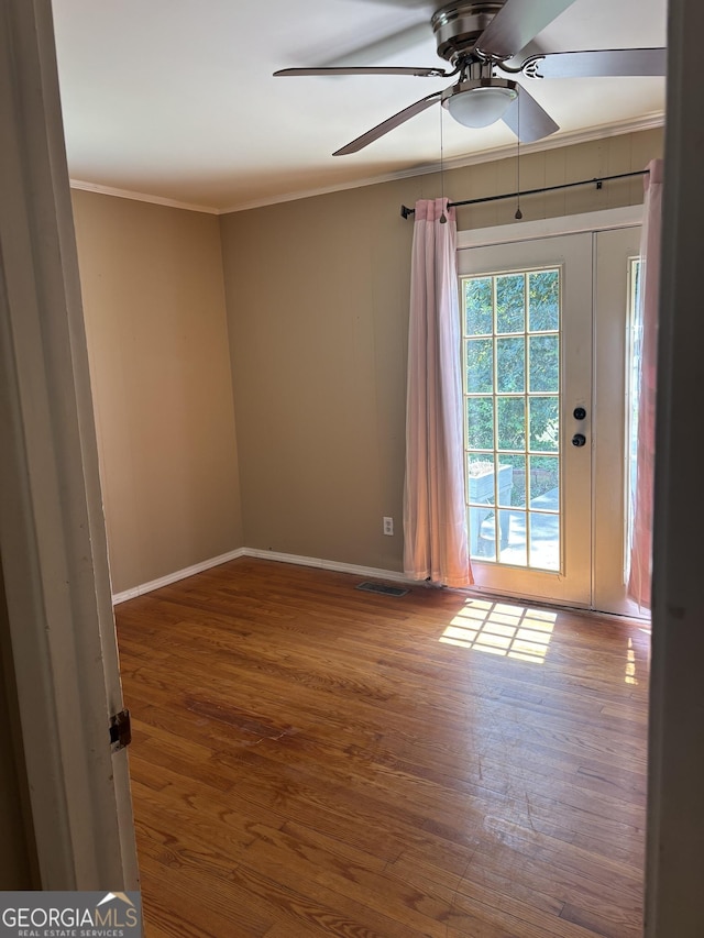spare room with wood finished floors, visible vents, crown molding, baseboards, and ceiling fan