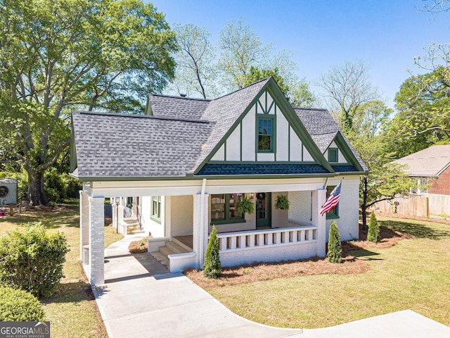 tudor house featuring a shingled roof, stucco siding, driveway, covered porch, and a front yard