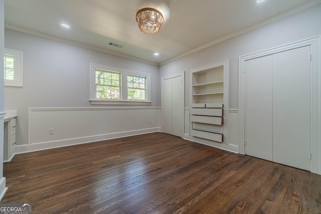 unfurnished bedroom with visible vents, ornamental molding, dark wood-type flooring, and two closets