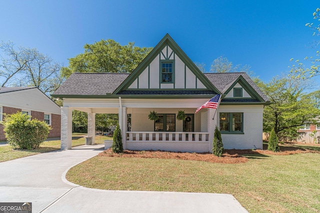 tudor house with brick siding, a porch, a shingled roof, and a front yard