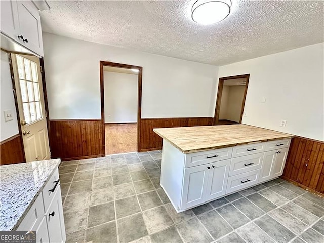 1836 Rainbow Ln, Powder Springs, GA 30127 - kitchen with white cabinetry, a textured ceiling, wainscoting, wooden walls, and butcher block counters