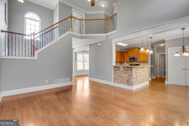 unfurnished living room featuring light wood-type flooring, a towering ceiling, baseboards, visible vents, and crown molding