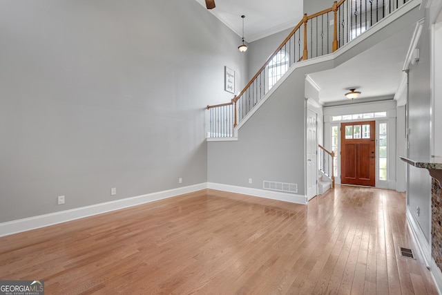 foyer entrance featuring light wood-type flooring, a towering ceiling, baseboards, stairs, and ornamental molding