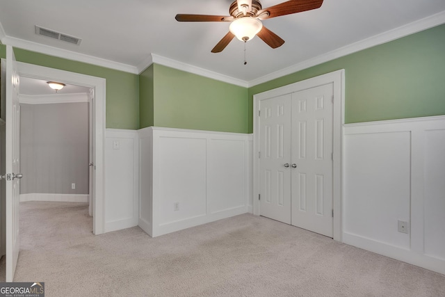 unfurnished bedroom featuring a decorative wall, wainscoting, carpet, ornamental molding, and visible vents