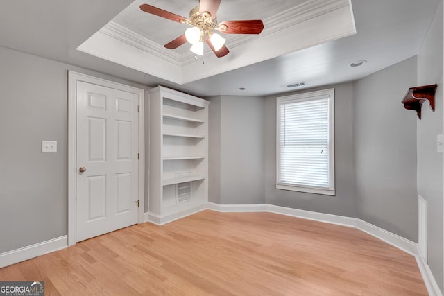 interior space featuring light wood-type flooring, baseboards, visible vents, ceiling fan, and a raised ceiling