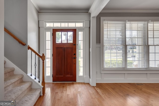 entrance foyer with a decorative wall, crown molding, stairs, light wood finished floors, and visible vents