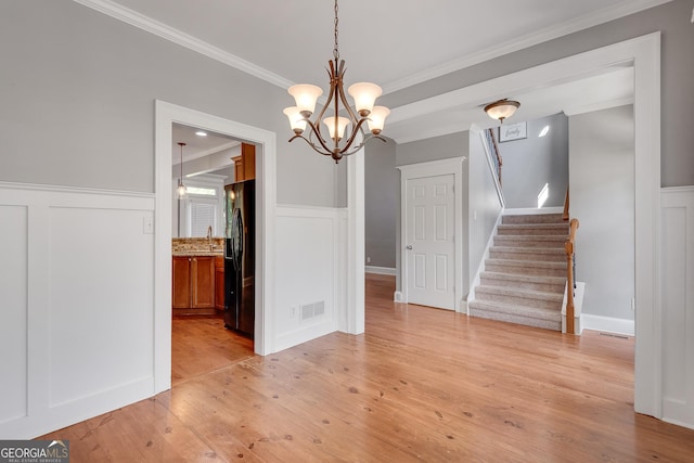 unfurnished dining area featuring light wood-style floors, a wainscoted wall, and ornamental molding