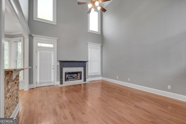 unfurnished living room featuring a high ceiling, a ceiling fan, light wood-style floors, and baseboards