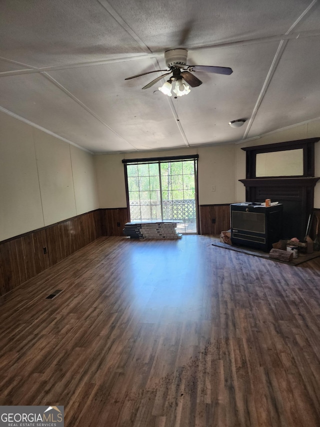 unfurnished living room featuring a ceiling fan, a wainscoted wall, wood finished floors, and wooden walls