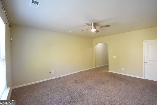 carpeted empty room with arched walkways, visible vents, a ceiling fan, and baseboards