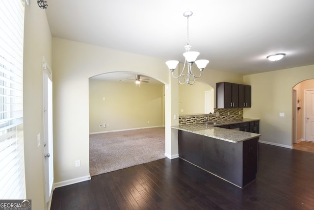 kitchen with a peninsula, dark wood-style floors, arched walkways, dark brown cabinetry, and backsplash