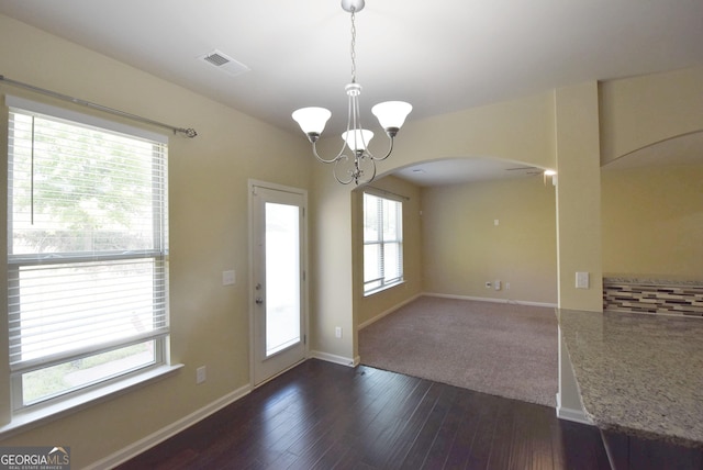 unfurnished dining area featuring arched walkways, an inviting chandelier, dark wood finished floors, baseboards, and visible vents