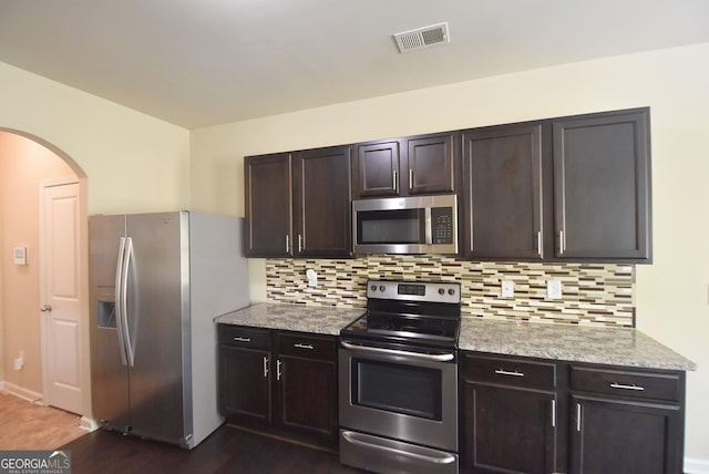 kitchen featuring decorative backsplash, arched walkways, stainless steel appliances, dark wood-type flooring, and visible vents
