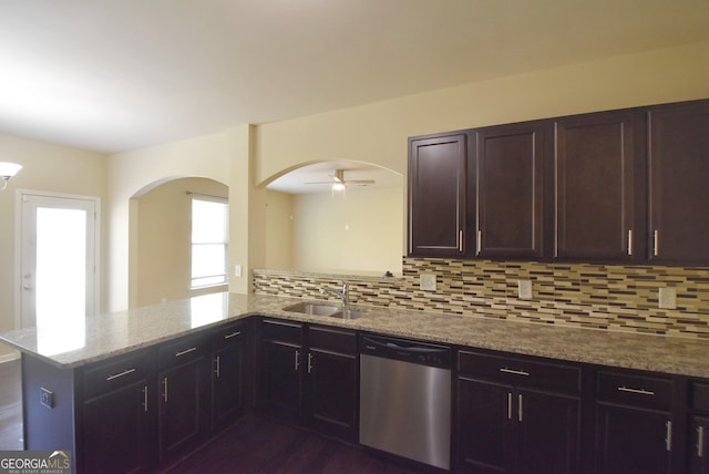 kitchen featuring tasteful backsplash, a sink, dishwasher, arched walkways, and light stone countertops