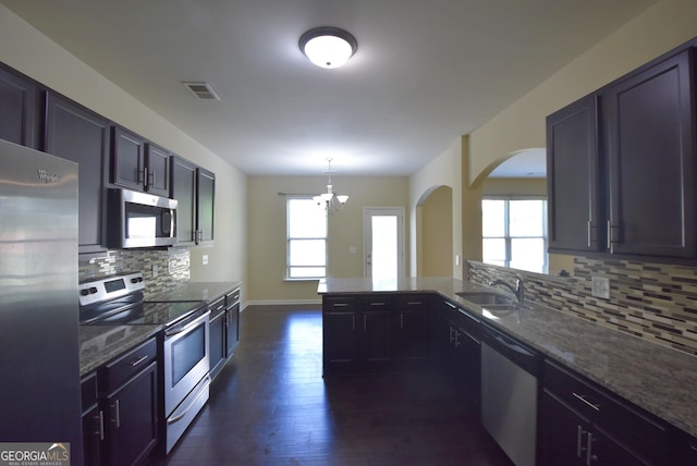 kitchen with arched walkways, a sink, tasteful backsplash, a notable chandelier, and appliances with stainless steel finishes