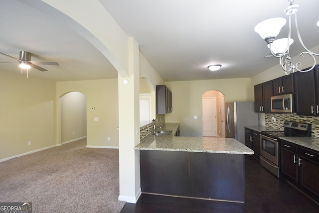 kitchen with arched walkways, baseboards, decorative backsplash, appliances with stainless steel finishes, and ceiling fan with notable chandelier