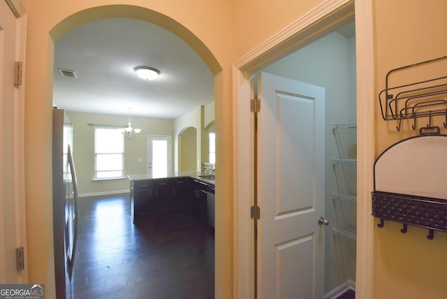 corridor with visible vents, arched walkways, a notable chandelier, and dark wood-style flooring