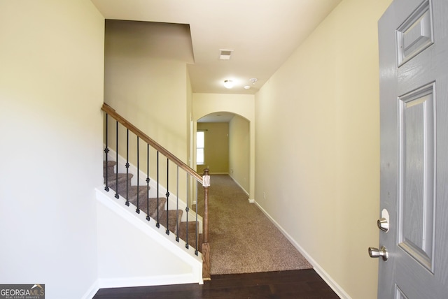 entryway featuring arched walkways, stairs, baseboards, and dark wood-style flooring